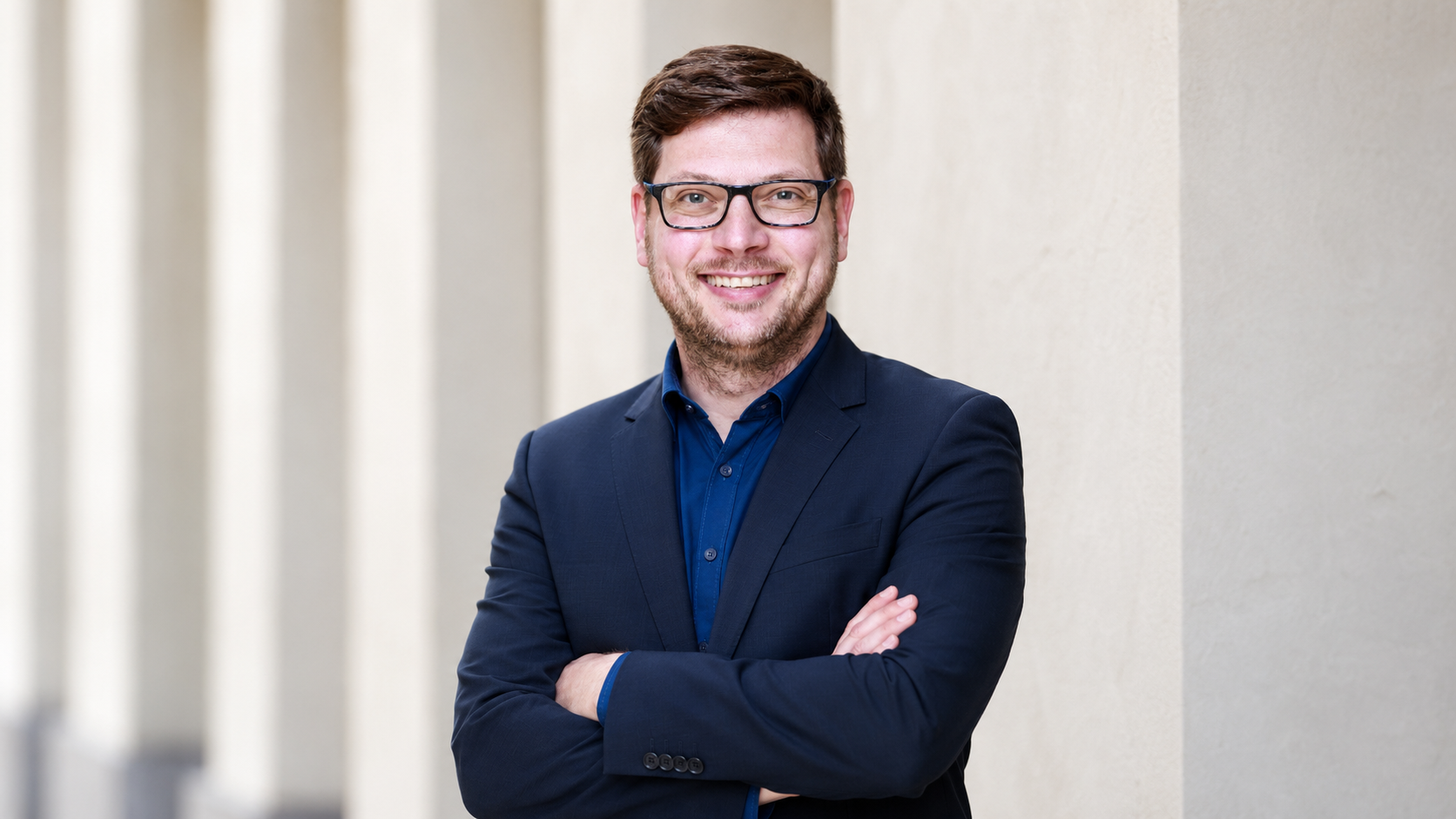 Porträt des Trainers Richard Röhlig mit Brille, blauem Hemd und dunklem Sakko vor einer hellen Fassade.