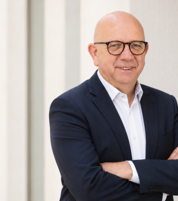 Porträt des Trainers Norbert Weiß mit Brille und weißem Hemd unter dunklem Sakko.