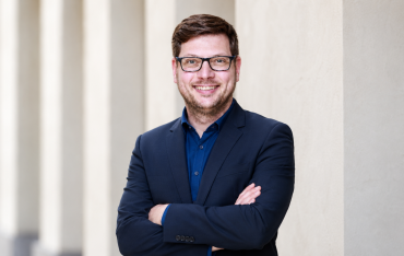 Porträt des Trainers Richard Röhlig mit Brille, blauem Hemd und dunklem Sakko vor einer hellen Fassade.