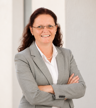 Porträt der Trainerin Sylvia Pfaff mit Brille und grauem Blazer vor einer hellen Außenwand.